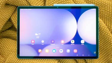 Samsung Galaxy Tab S10 Plus with stylus attached to the edge, display on, sitting on a yellow blanket