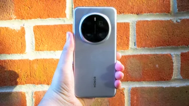 Honor Magic 7 Pro in hand in front of a red brick wall, rear view