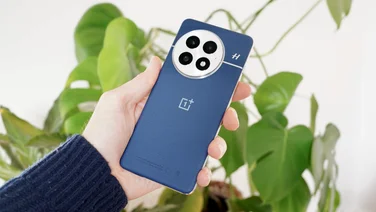 OnePlus 13 in hand, rear view, in front of some plants