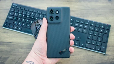 Motorola Thinkphone 25 in hand, rear view, in front of a mouse and keyboard