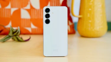 Samsung Galaxy S25 rear view, standing in front of an orange bag and yellow jug
