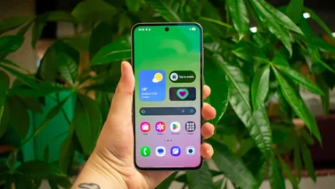 Samsung Galaxy A56 in hand in front of a plant, front view with the display on