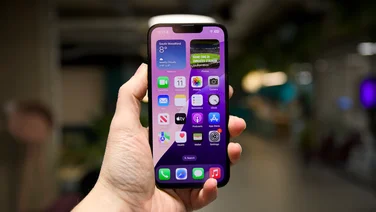 The iPhone 16e pictured in hand from the front in an office environment