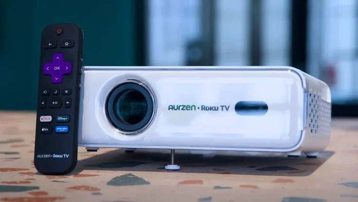 The Aurzen Eazze 1DR Roku projector and its remote on a work surface