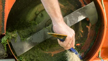 6 ways to refresh your lawn mower for spring someone cleaning the bottom of a lawn with a brush