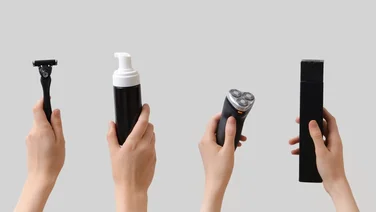 Electric shaver vs razor, a razor, shaving foam bottle and electric shaver being held in the air