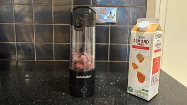 Frozen berries in the Nutribullet Portable with a carton of almond milk on the side