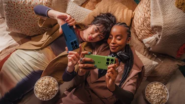 Two people lying next to each other, holding up their Motorola Edge 60 phones