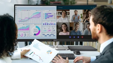 Two business multiracial partners, a man and a woman, are sitting in a modern office, in front of a computer screen, conducting online brainstorm for an international group of company employees using a Philips monitor