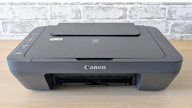 The Canon Pixma MG2551S pictured from the font on a wood desk with the lid closed