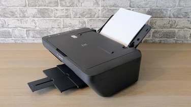 The Canon Pixma MG2551S pictured on a desk from an angle with its paper input tray filled