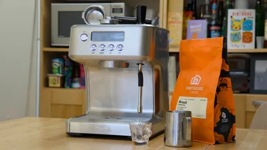 The ProCook Espresso Coffee Machine pictured on a kitchen table with a bag of coffee and a milk steaming jug