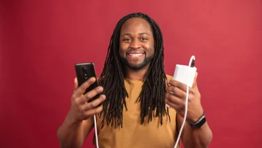 Happy man holding power bank connected to smartphone - red background behind