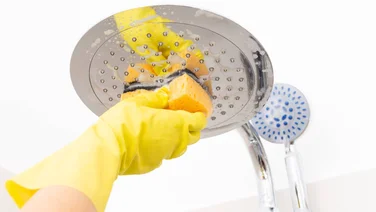 Metallic shower head being cleaned with orange sponge