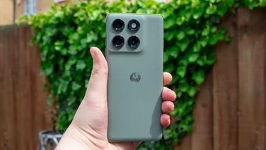 Motorola Edge 60 Pro in hand, rear view, in front of an ivy-covered fence
