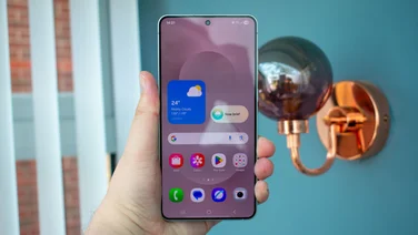 Samsung Galaxy S25 Edge in hand, display on, in front of a light fixture and open blinds
