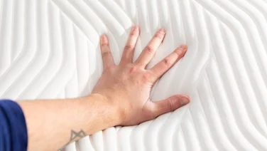 A hand pressing into the surface of a mattress