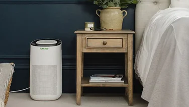 Do air purifiers dry the air Meaco next to a bedside table in a bedroom