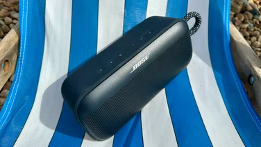 The Bose SoundLink Plus Bluetooth speaker on a white and blue deckchair