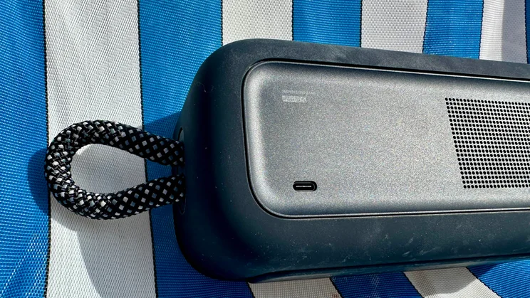 Close-up of the USB-C port and carrying strap of a Bose SoundLink Plus resting on a blue and white deckchair