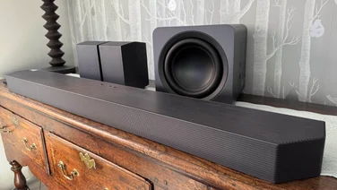 Angled view of the Samsung HW-Q990F soundbar, subwoofer and rear speakers on a wooden dresser