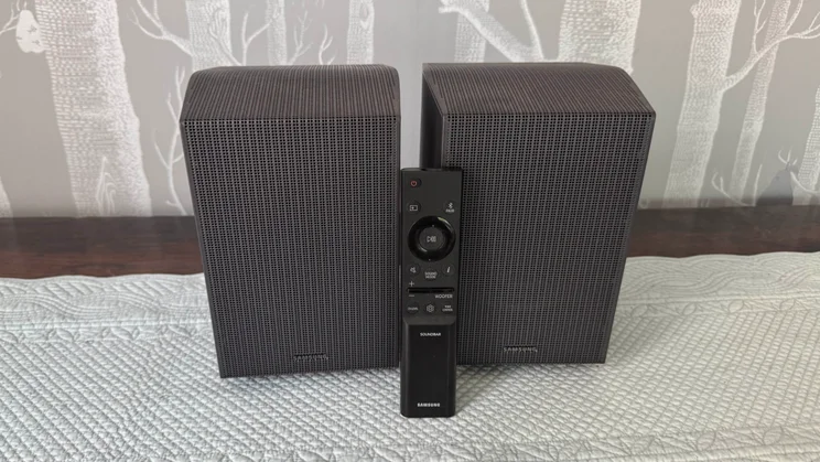 The pair of rear speakers included as part of the Samsung HW-Q990F home audio system with the remote control resting against them