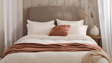 Bed dressed with white linen bedding and terracotta throw