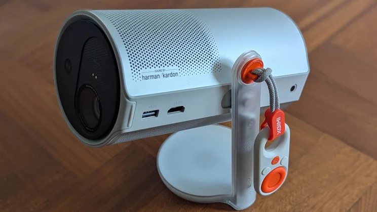 The XGIMI MoGo 4 portable projector on a wooden floor with its mini remote attached to a lanyard