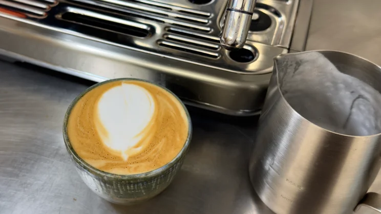 A cup of coffee, next to the drip tray of the Sage Barista Touch Impress