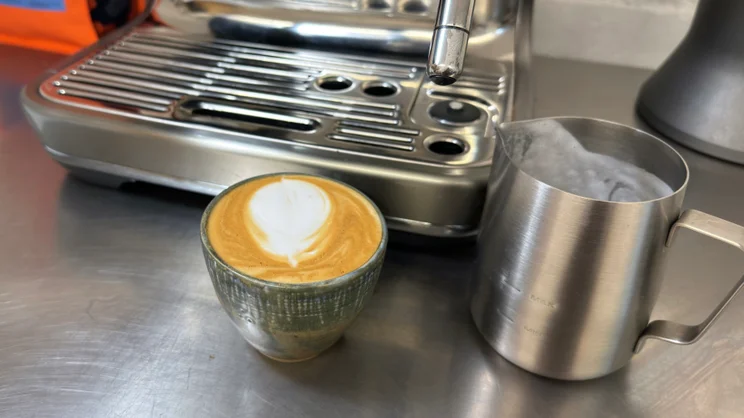 A cup of coffee, next to the drip tray of the Sage Barista Touch Impress