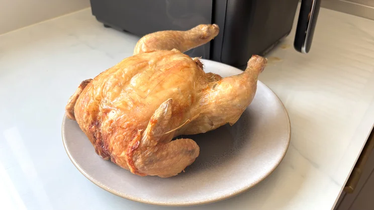 A cooked chicken on a plate, alongside the Tower Vortx 11 Litre Dual Layer air fryer