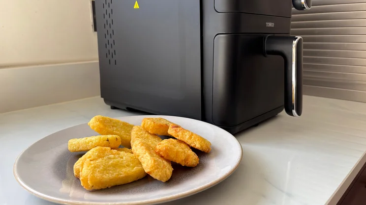 A plate of cooked hash browns alongside the Tower Vortx 11 Litre Dual Layer air fryer