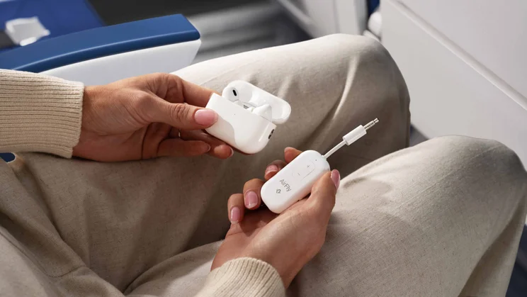 A woman on an aeroplane holding the Twelve South AirFly Pro 2 adapter and a pair of AirPods in their case