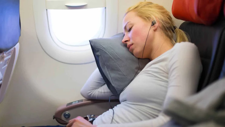 A blonde lady sleeping on an aeroplane with the in-flight headphones in her ears