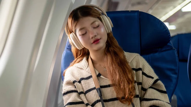 An Asian woman sleeping on an aeroplane while wearing noise-cancelling headphones