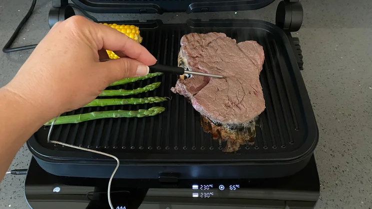 Steak grilling on the Zwilling Enfinigy Contact Grill. A hand is using the in-built thermometer probe to take its core temperature