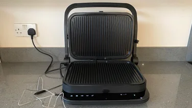 The Zwilling Enfinigy Contact Grill, open, on a kitchen countertop. A thermometer probe is attached to the side