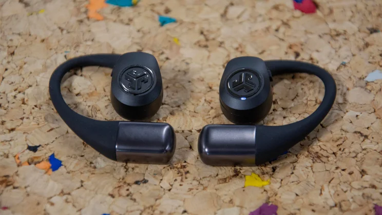 The JLab Epic Open Sport open-ear headphones laid flat on a cork table with their earhooks facing towards each other