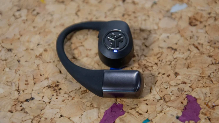 One of the JLab Epic Open Sport open-ear headphones laid flat on a cork table