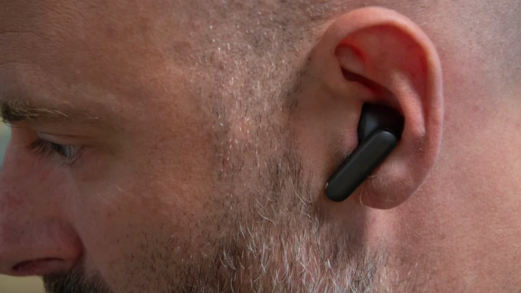 Close-up of the left earbud of the OnePlus Buds 4 being worn by a middle-aged man