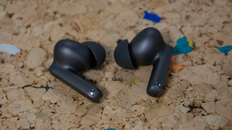 The OnePlus Buds 4 on a cork table with their earbud stems pointing downwards