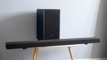 The Sharp HT-SBW55121 soundbar and subwoofer on a table with three wooden legs