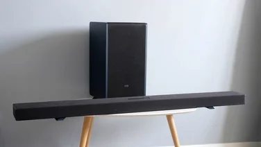 The Sharp HT-SBW55121 soundbar and subwoofer on a table with three wooden legs