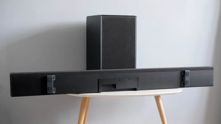 The Sharp HT-SBW55121 soundbar and subwoofer on a table with three wooden legs, with the soundbar turned on its side
