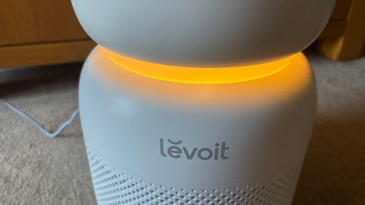 A closeup of the Levoit Sprout air purifier, showing the Levoit logo. The unit is glowing orange