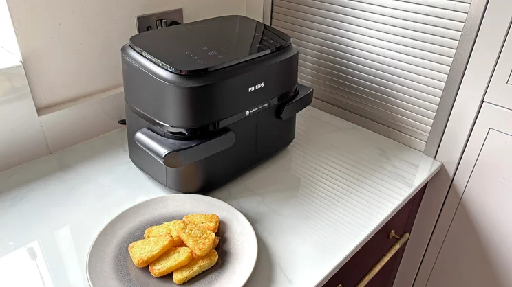 The Philips 1000 Series air fryer on a kitchen worktop next to a plate of cooked hash browns
