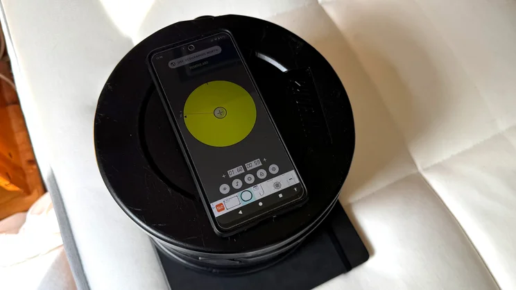 On the surface of the REM-Fit Natural Lux Hybrid mattress, a series of weights are being used to test tilt degree at the edge of the mattress. A smartphone displays tilt readings