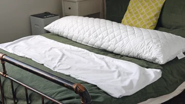 The Silentnight Body Support Pillow on a bed, next to its pillow case