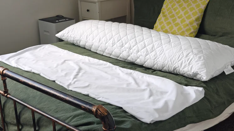 The Silentnight Body Support Pillow on a bed, next to its pillow case