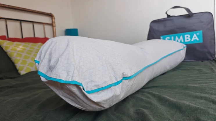 The Simba Body Pillow on a bed, with the pillow's carry bag in the background